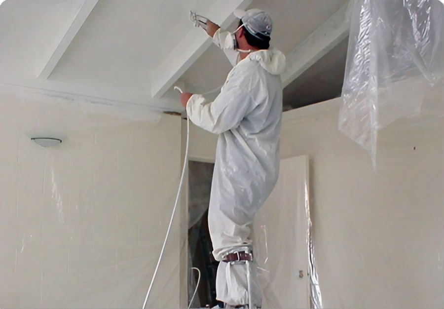 A man wearing protective gear is painting a ceiling white.