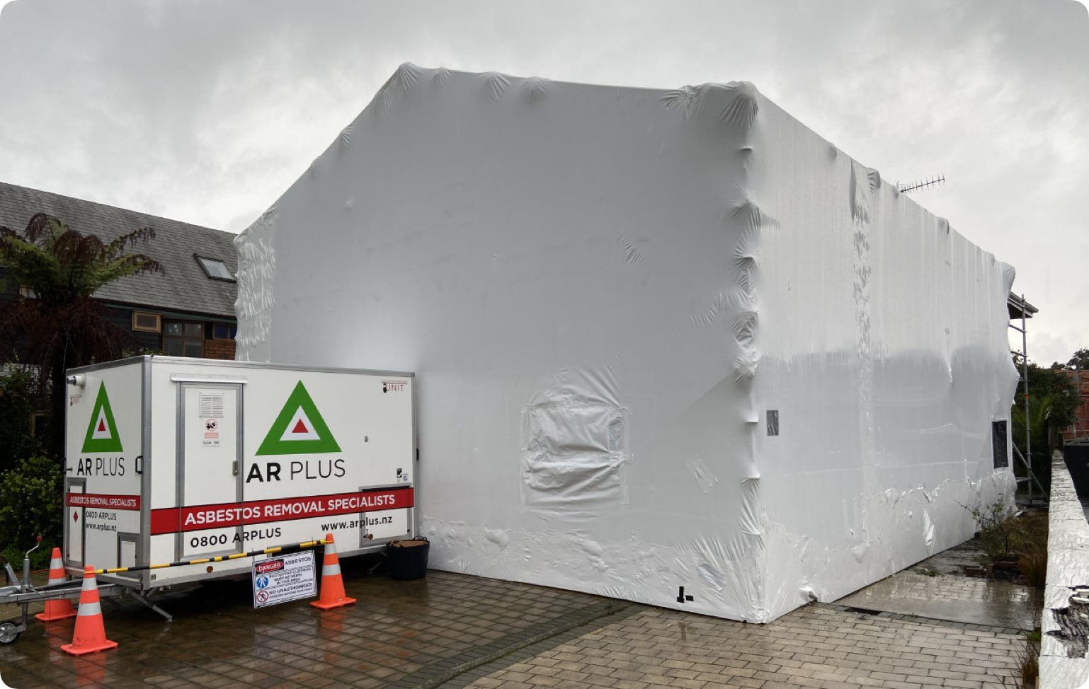 Building wrapped in white plastic undergoing asbestos removal by AR Plus.