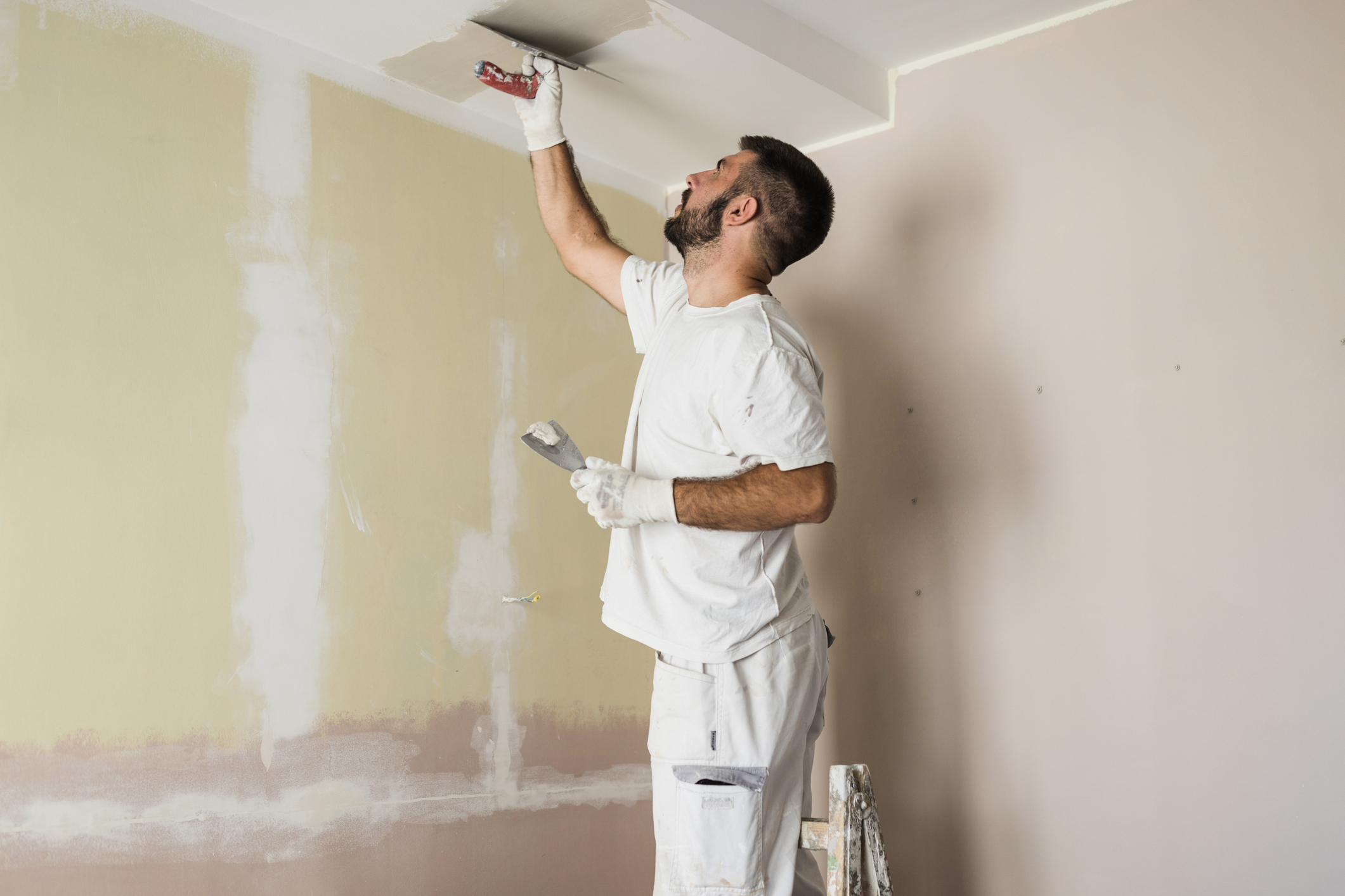 A man wearing white overalls paints a ceiling